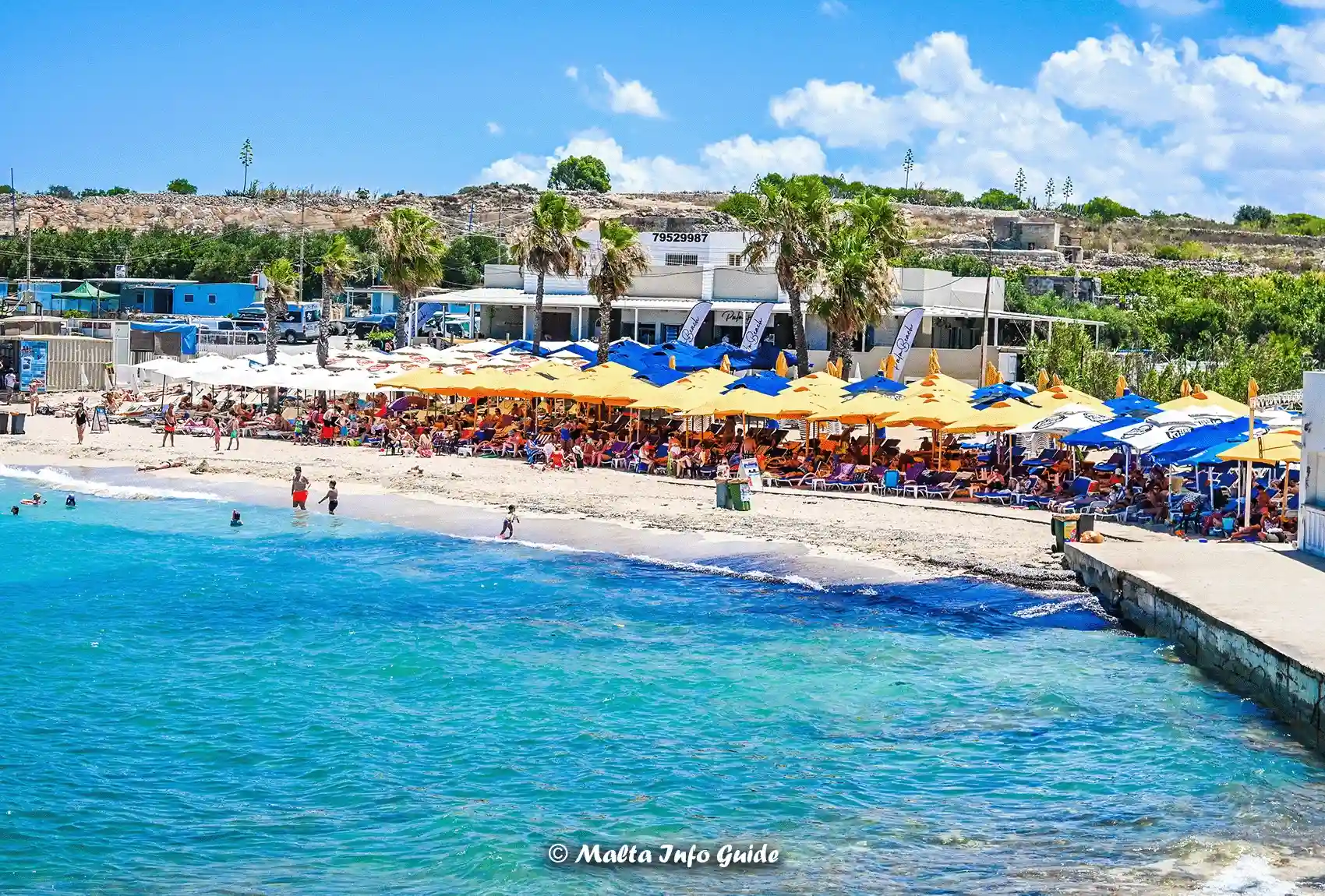 Beach umbrellas and lidos lining the Armier Bay shore.