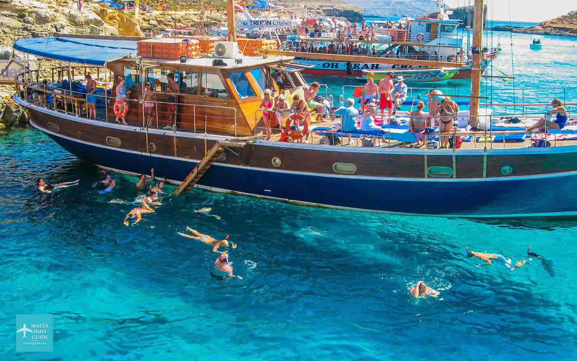 People swimming and standing on one of the boats moored at Comino island.