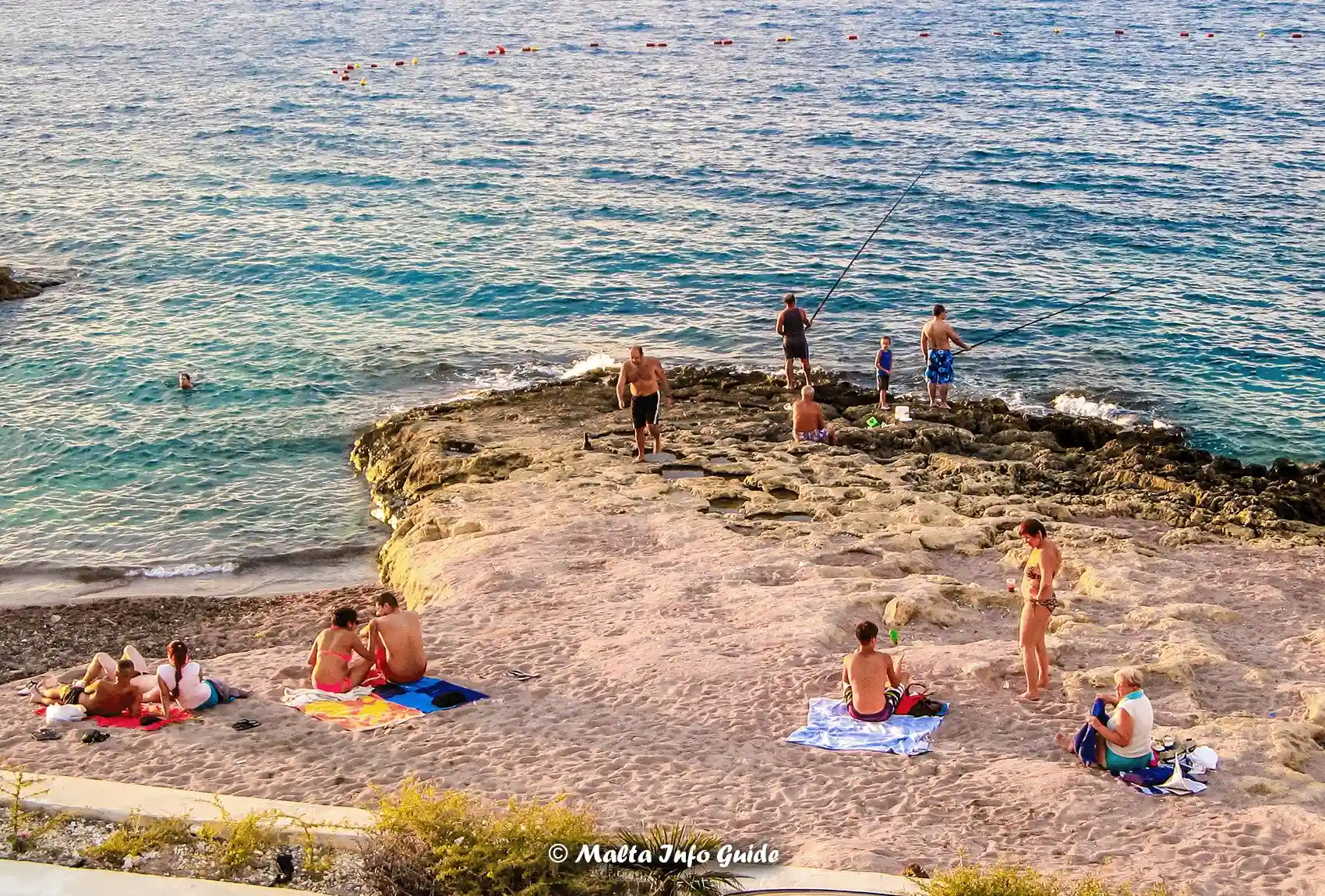 Swimmers and fishermen beside Bugibba Perched Beach rocks.