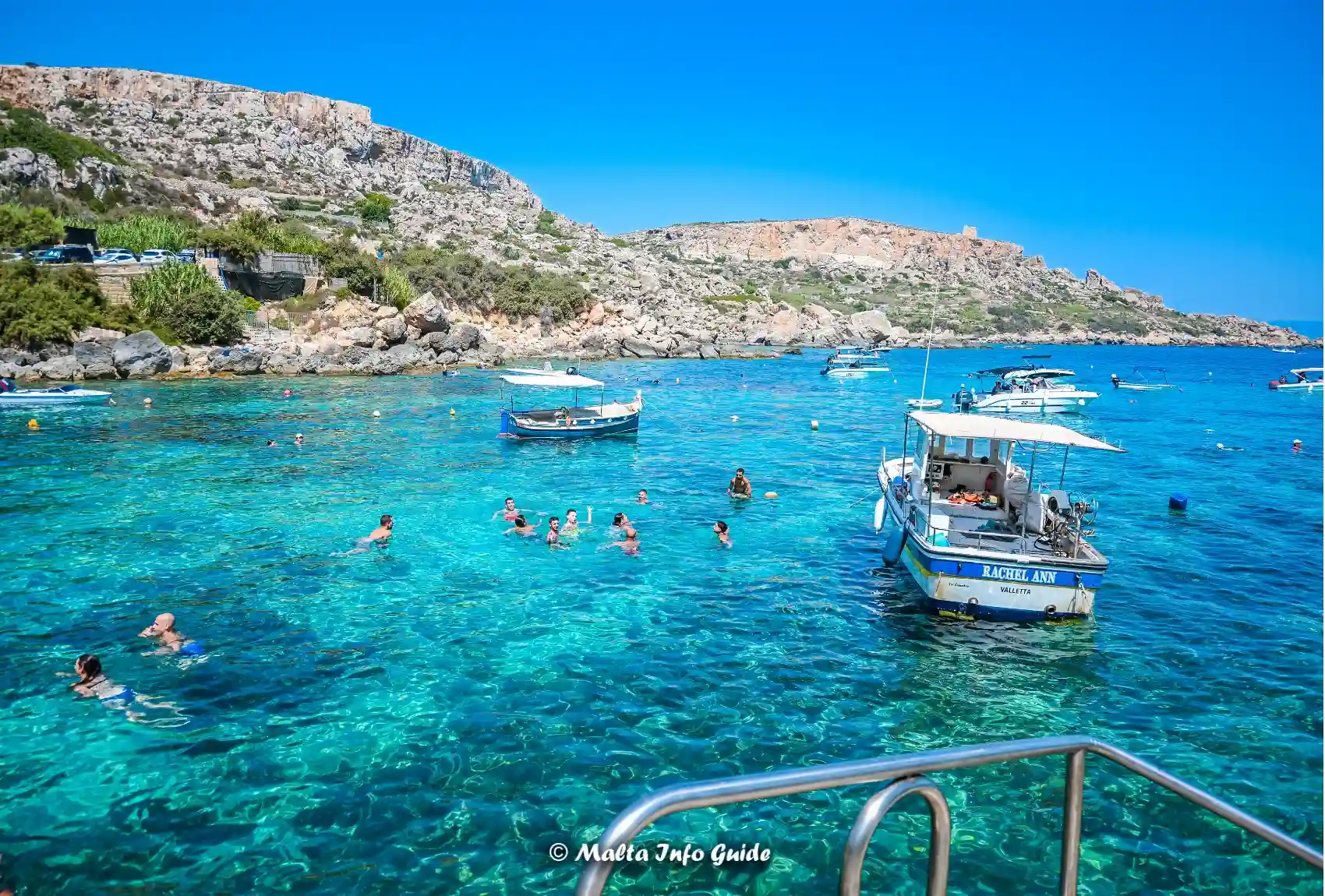 Boats and swimmers in turquoise water at Dahlet Qorrot.