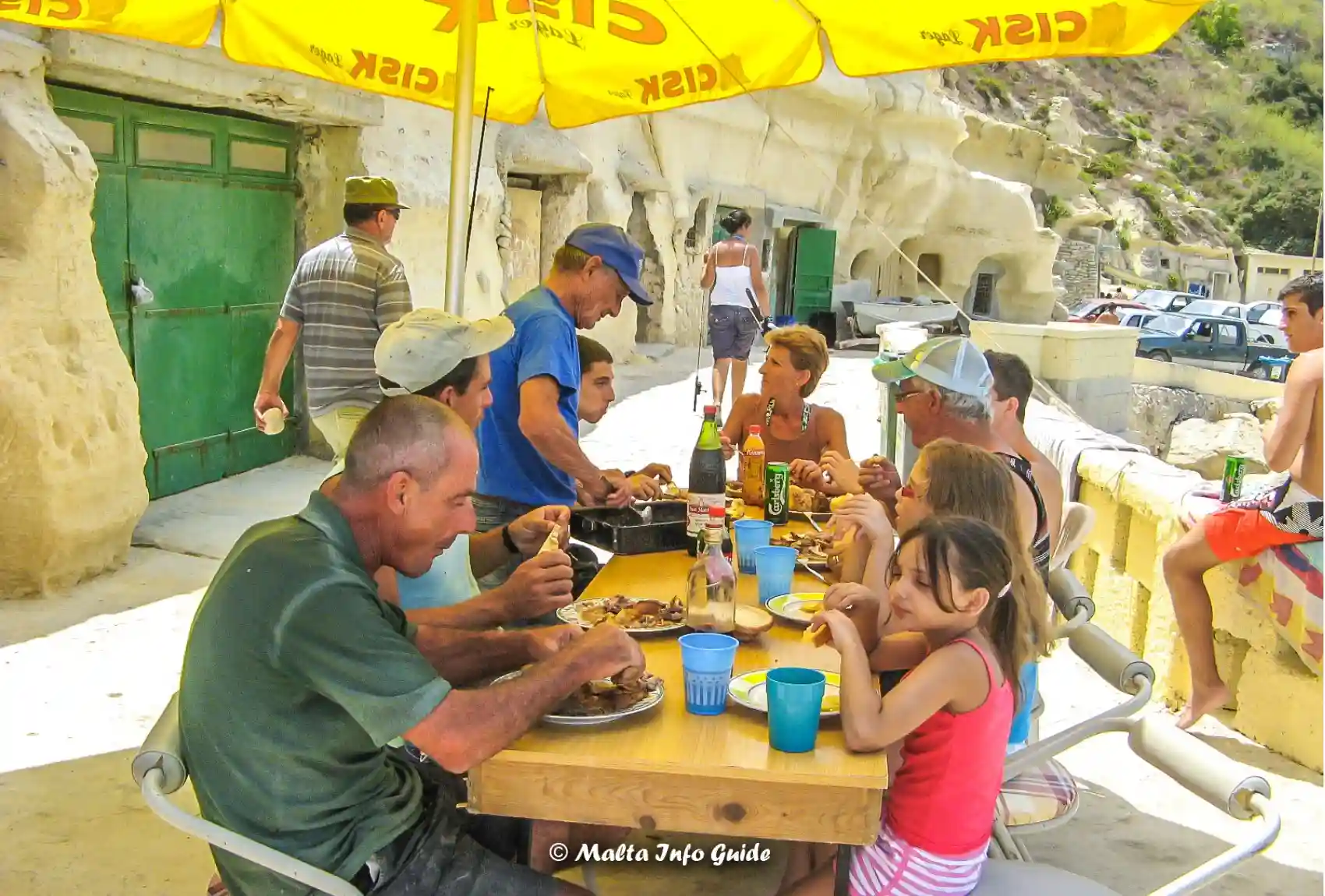 Family eating lunch beside rock-cut boathouses at Dahlet Qorrot.