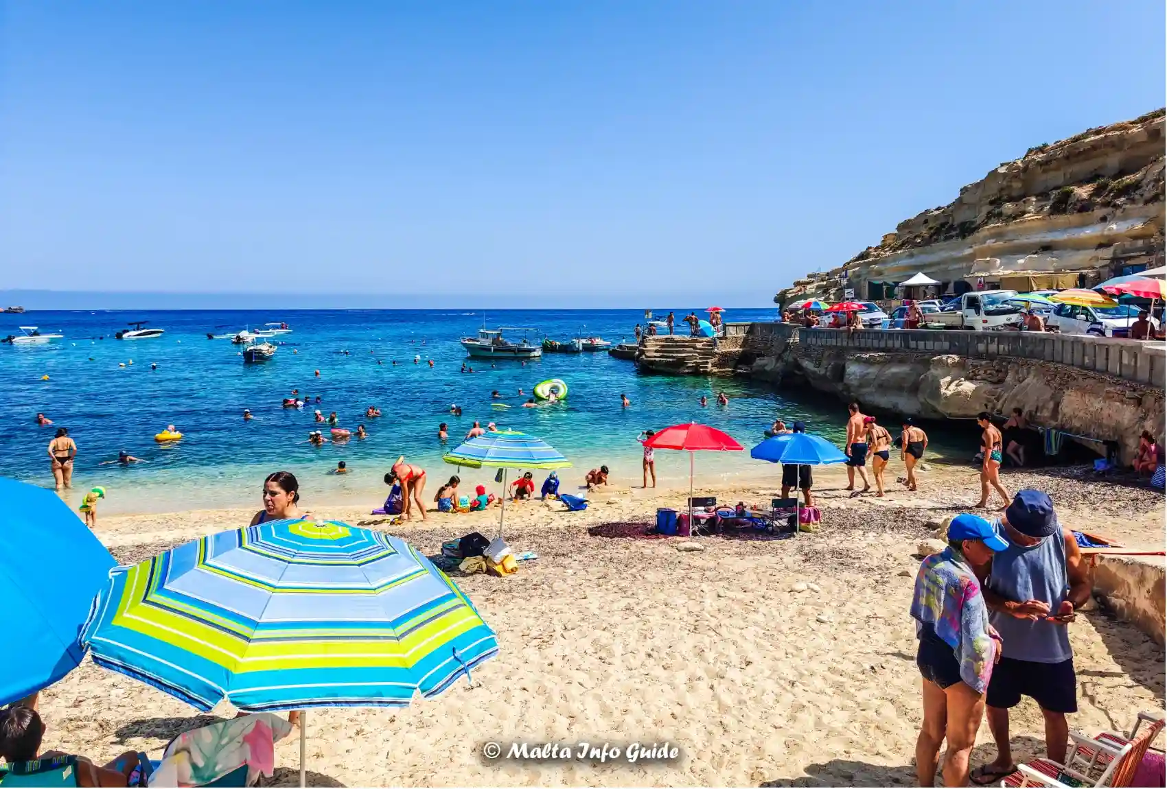 Beach umbrellas and swimmers at Dahlet Qorrot sandy shore.