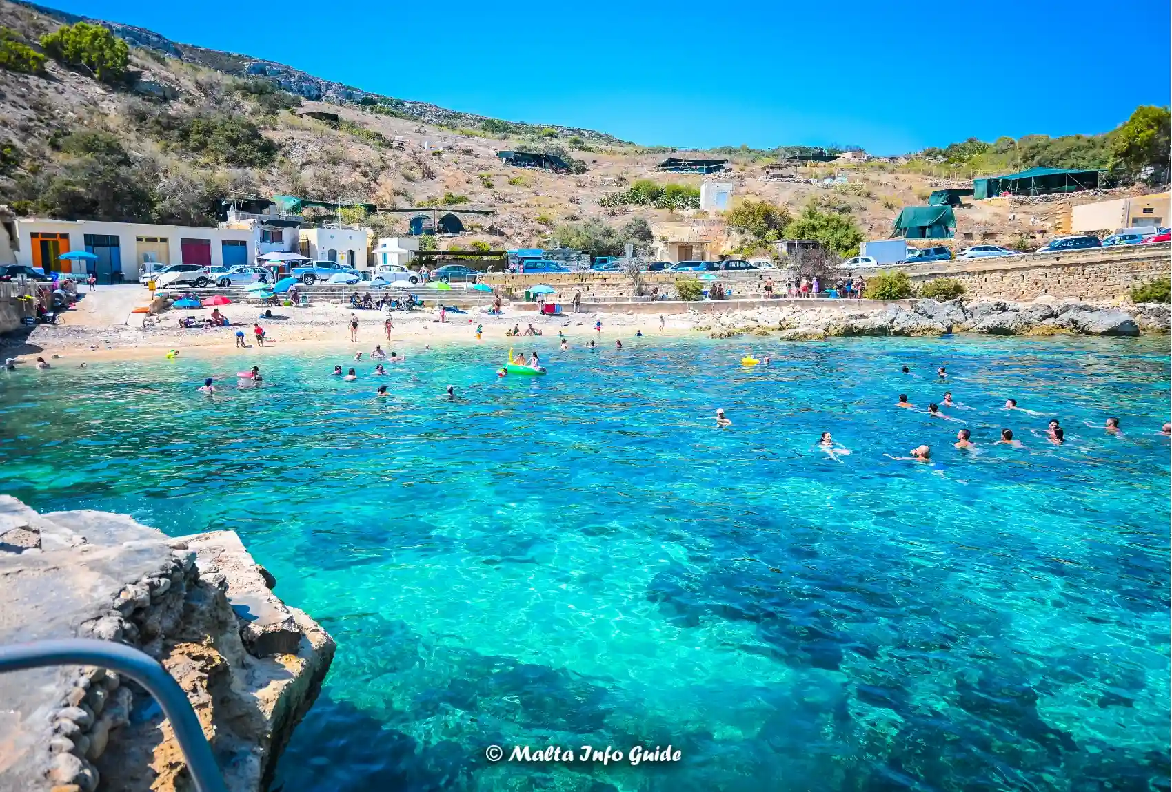Swimmers fill Dahlet Qorrot Bay beside small sandy beach.