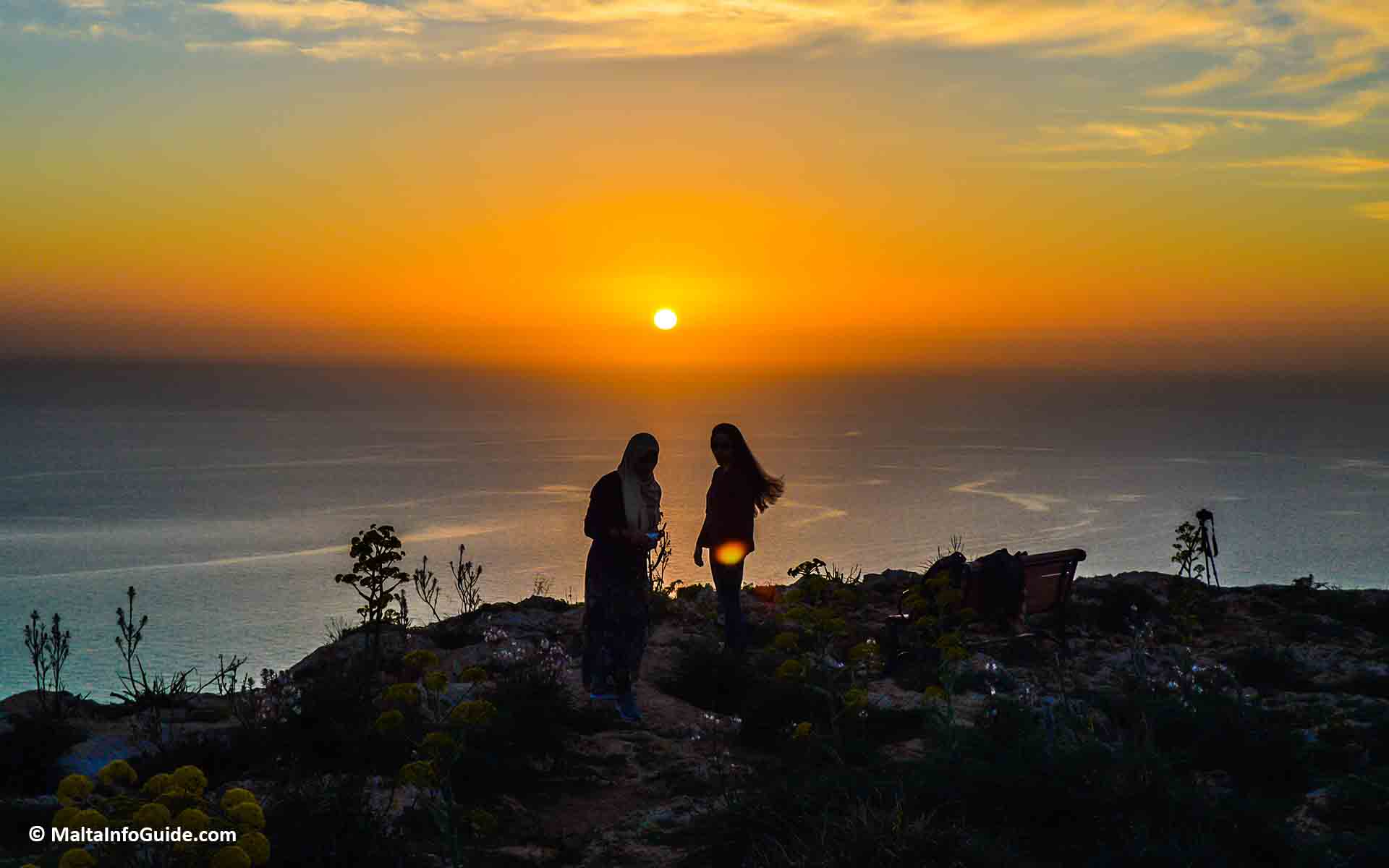 Two people sitting on the cliff at Dingli Cliffs during sunset.