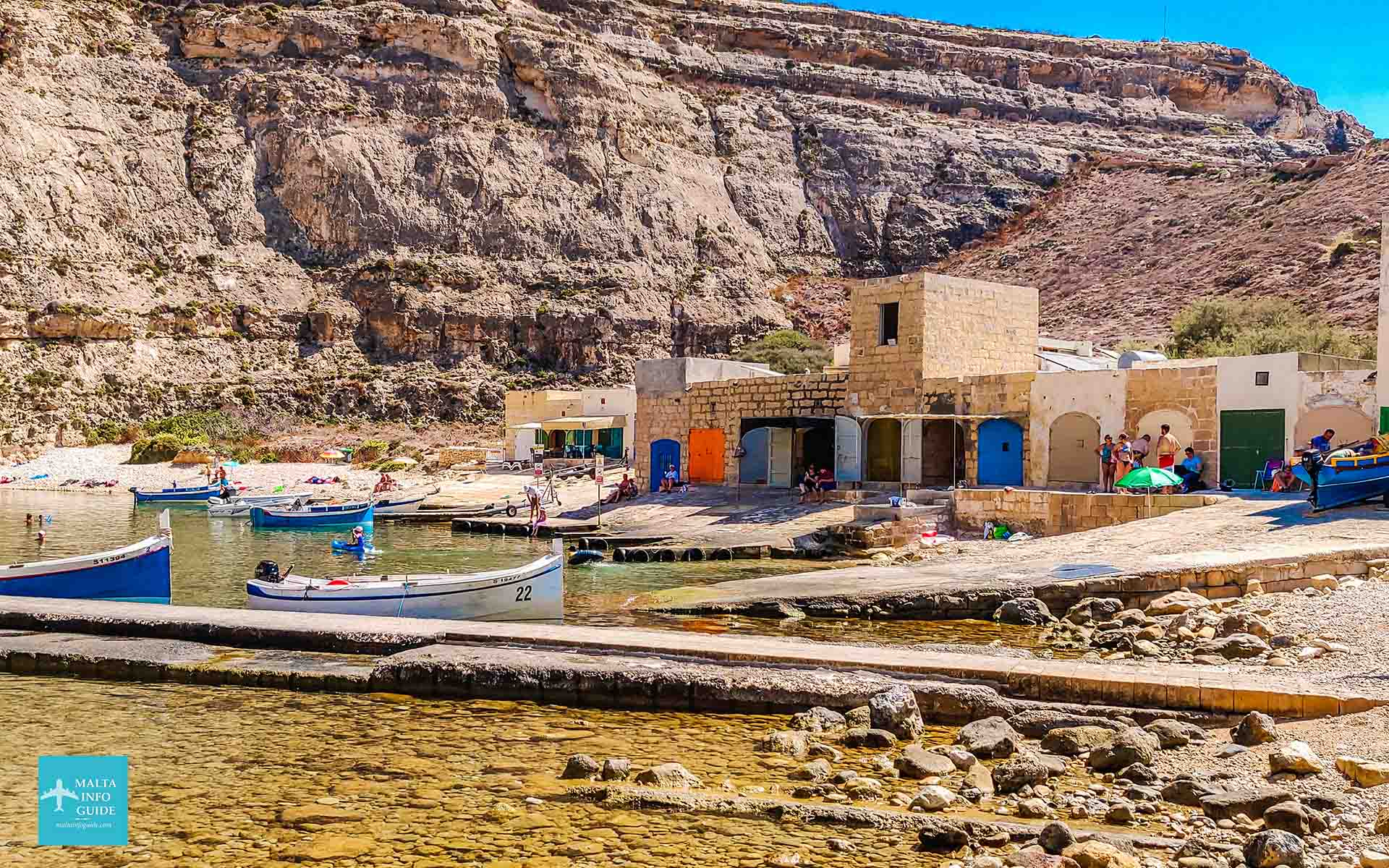 Boats rest in Dwejra Inland Sea beneath limestone cliffs.