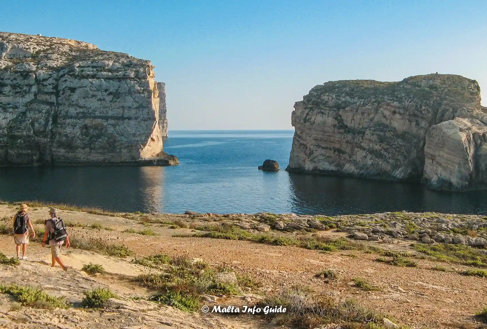 People hiking at sunset on the coastline of Dwejra Bay overlooking the Fungus Rock in Gozo.