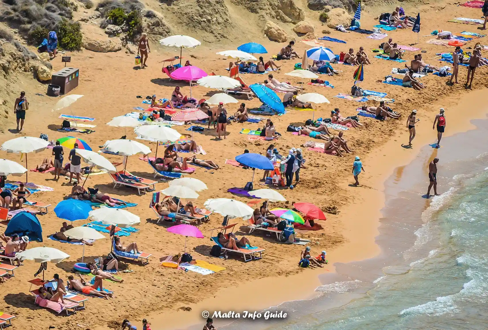 Visitors relax under umbrellas on Għajn Tuffieħa beach.