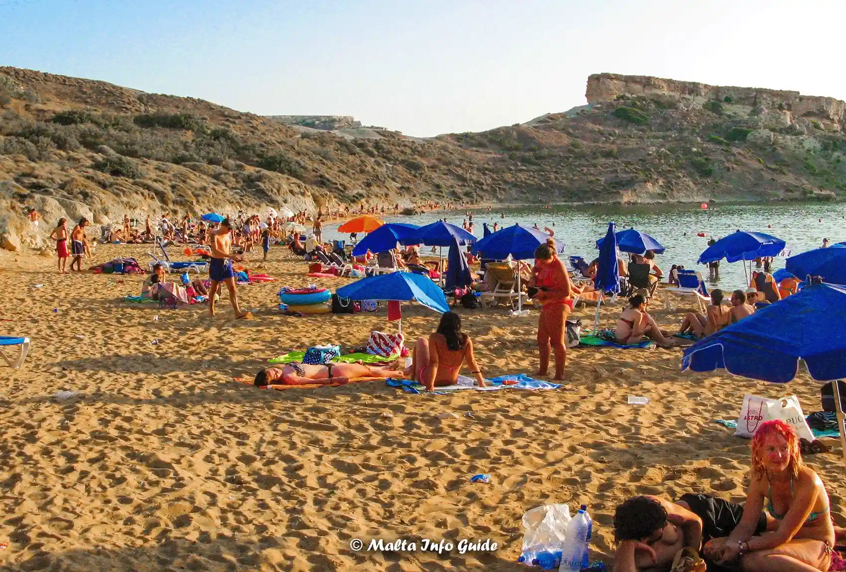 Beachgoers relax on sandy Għajn Tuffieħa Bay shore.