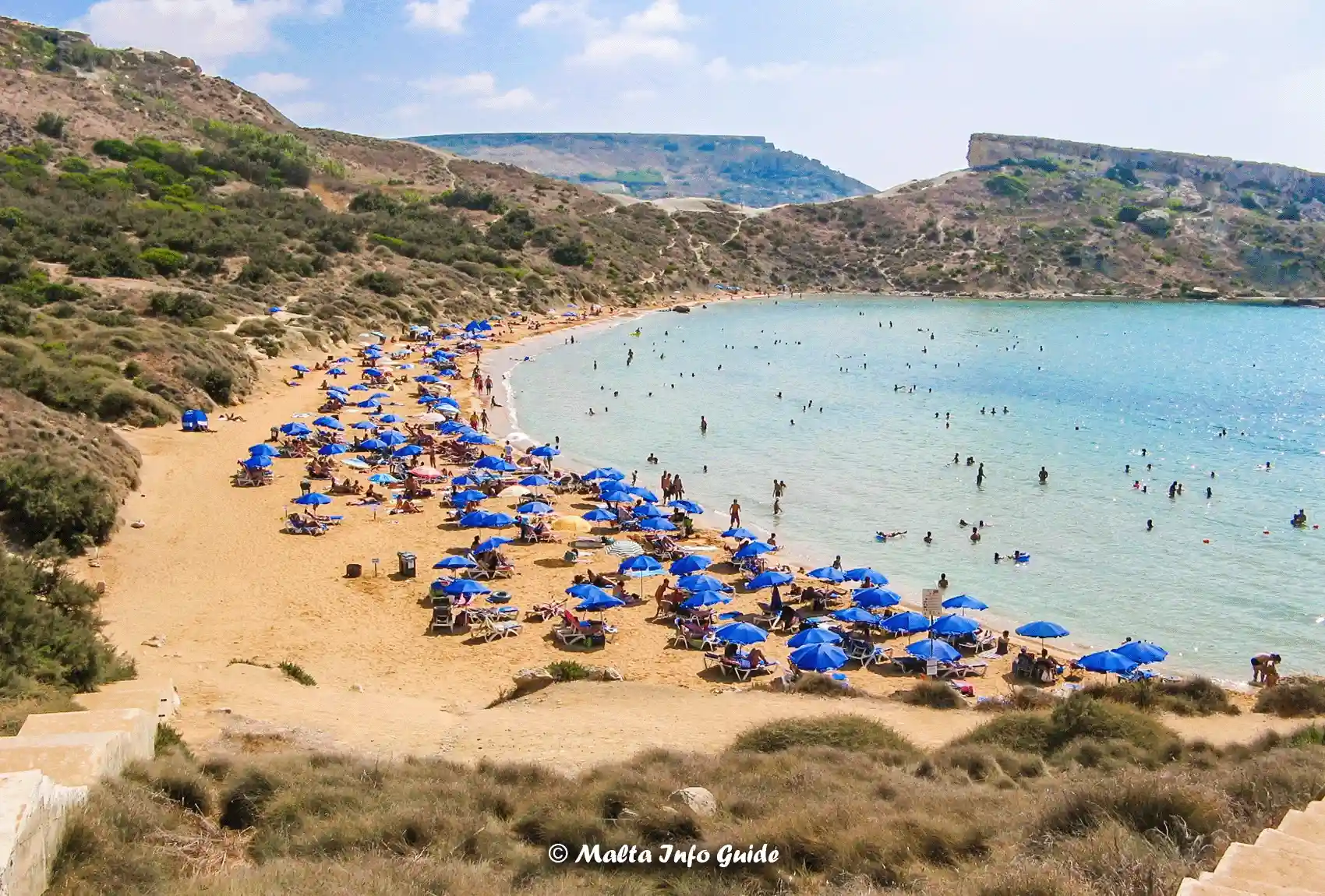 Blue sunbeds line sandy Għajn Tuffieħa Bay beach.