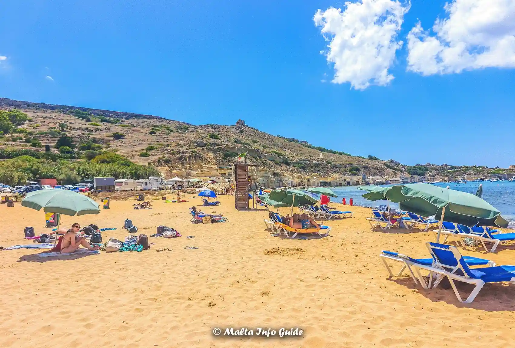 Sunbeds and umbrellas across Gnejna Bay sandy beach.