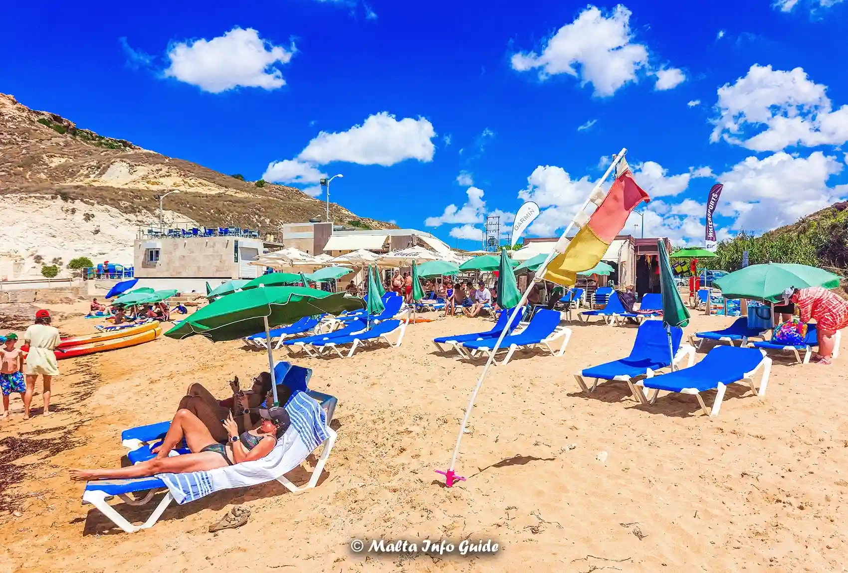 Sunbeds and umbrellas beside Gnejna Bay beach facilities.