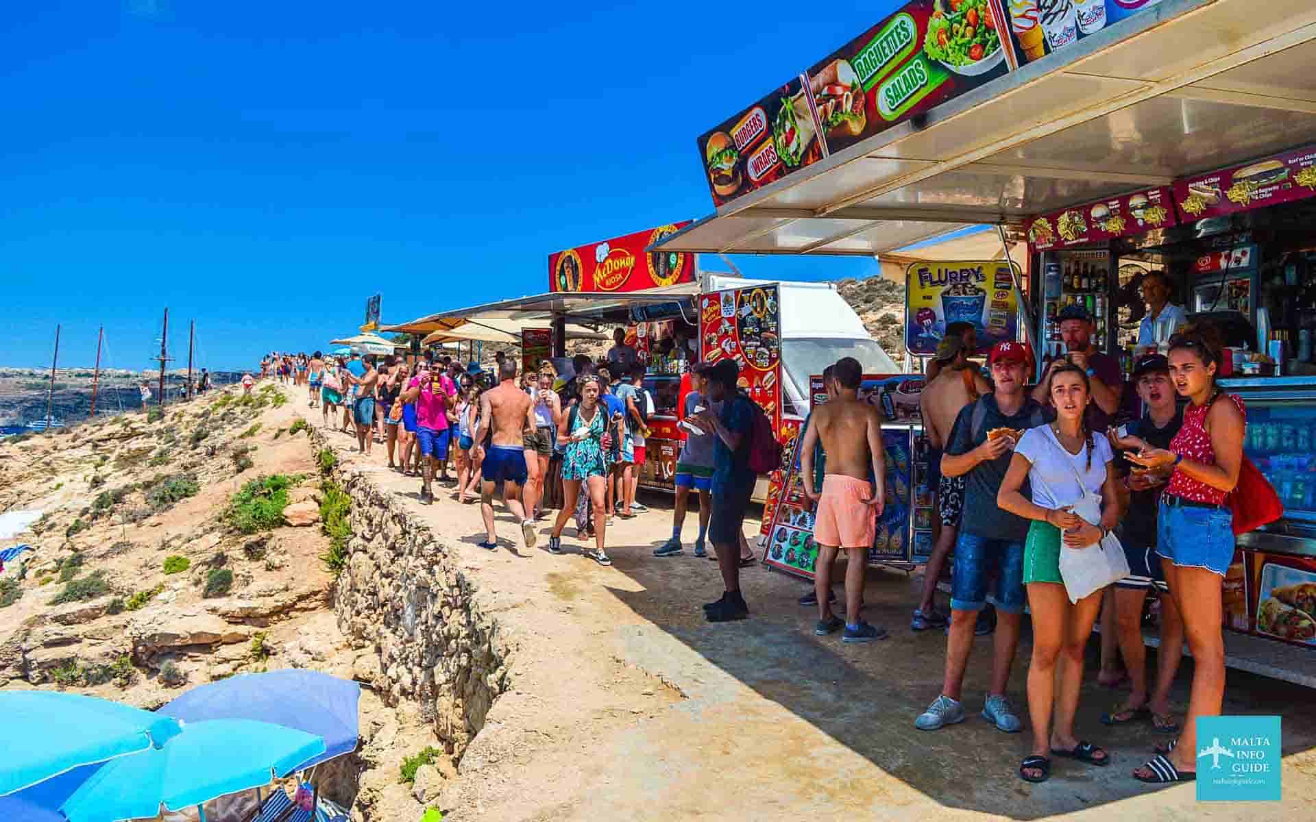 People walking by food kiosks that can be found on the island of Comino.