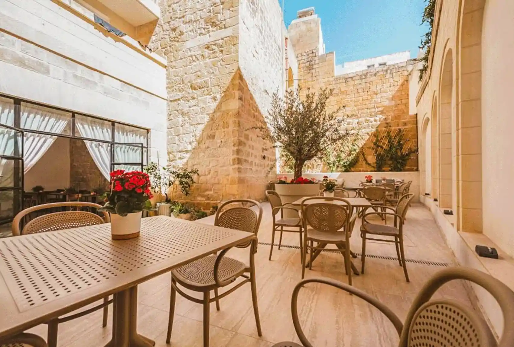 Warm stone walls, café tables, surround the courtyard of Maria Rosa Suites, Victoria, Gozo, Malta.