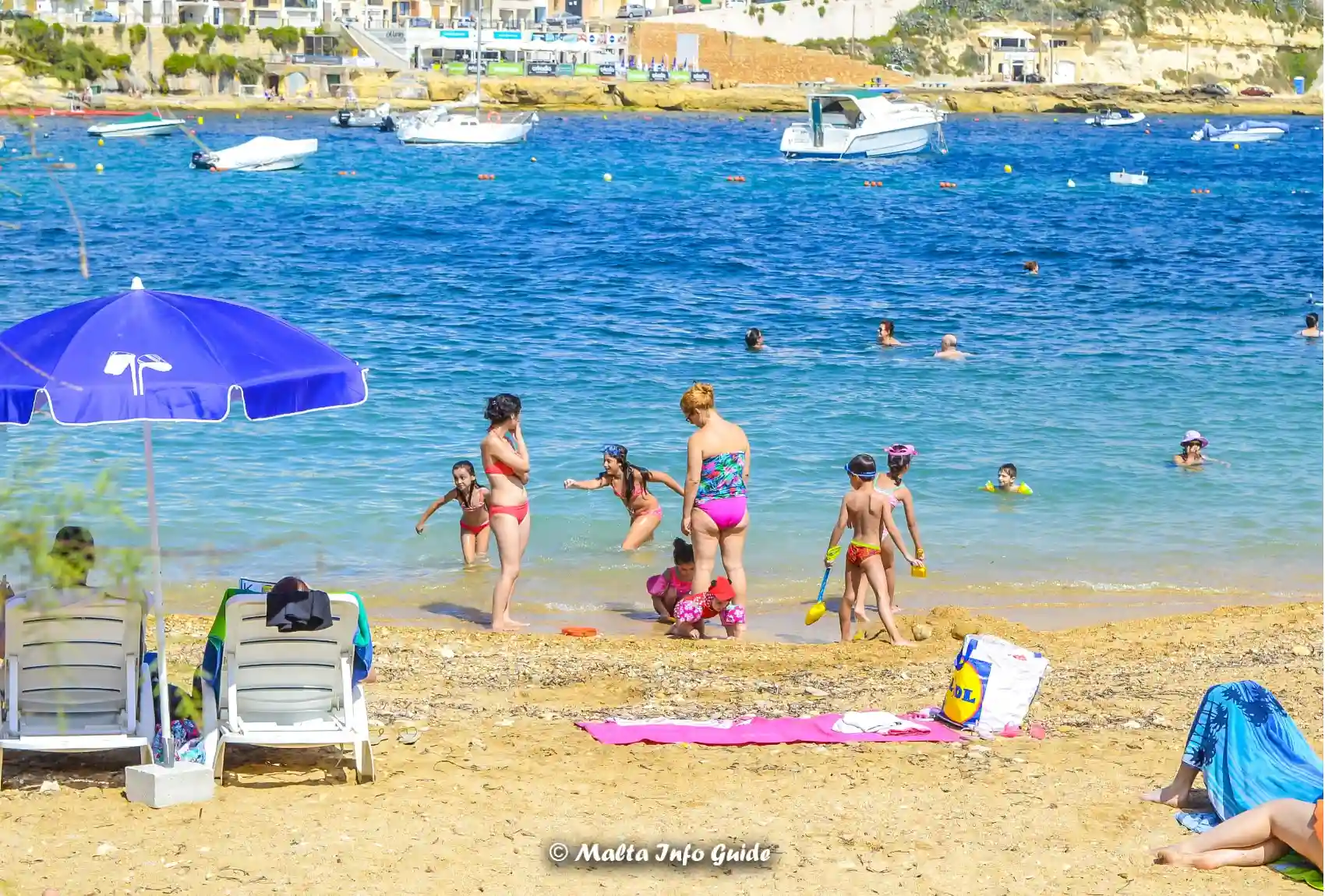 Families swimming from sandy Marsalforn Bay beach in Gozo.
