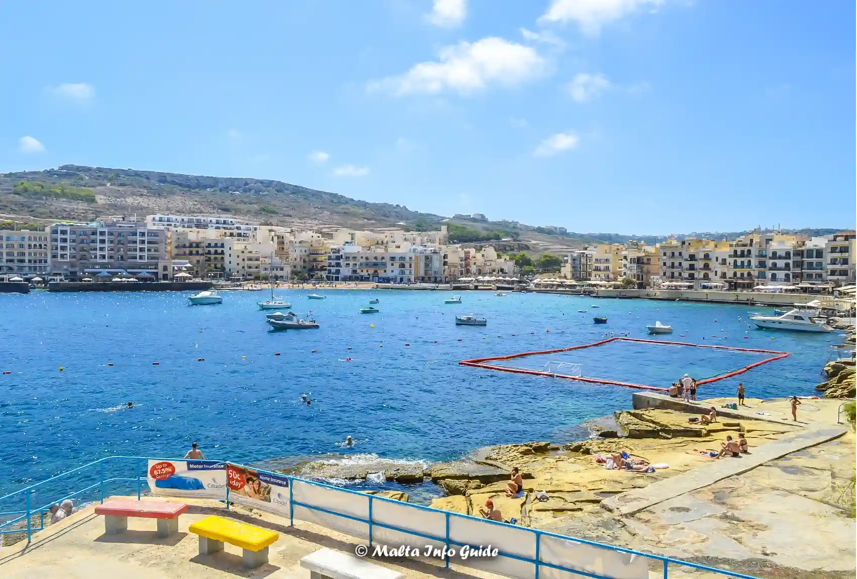 Rocky swimming area overlooking boats across Marsalforn Bay.