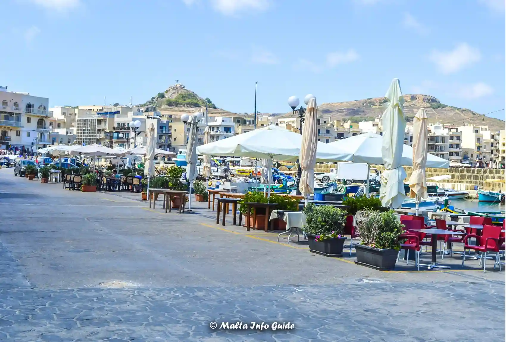 Outdoor restaurants beside fishing boats along Marsalforn harbour.