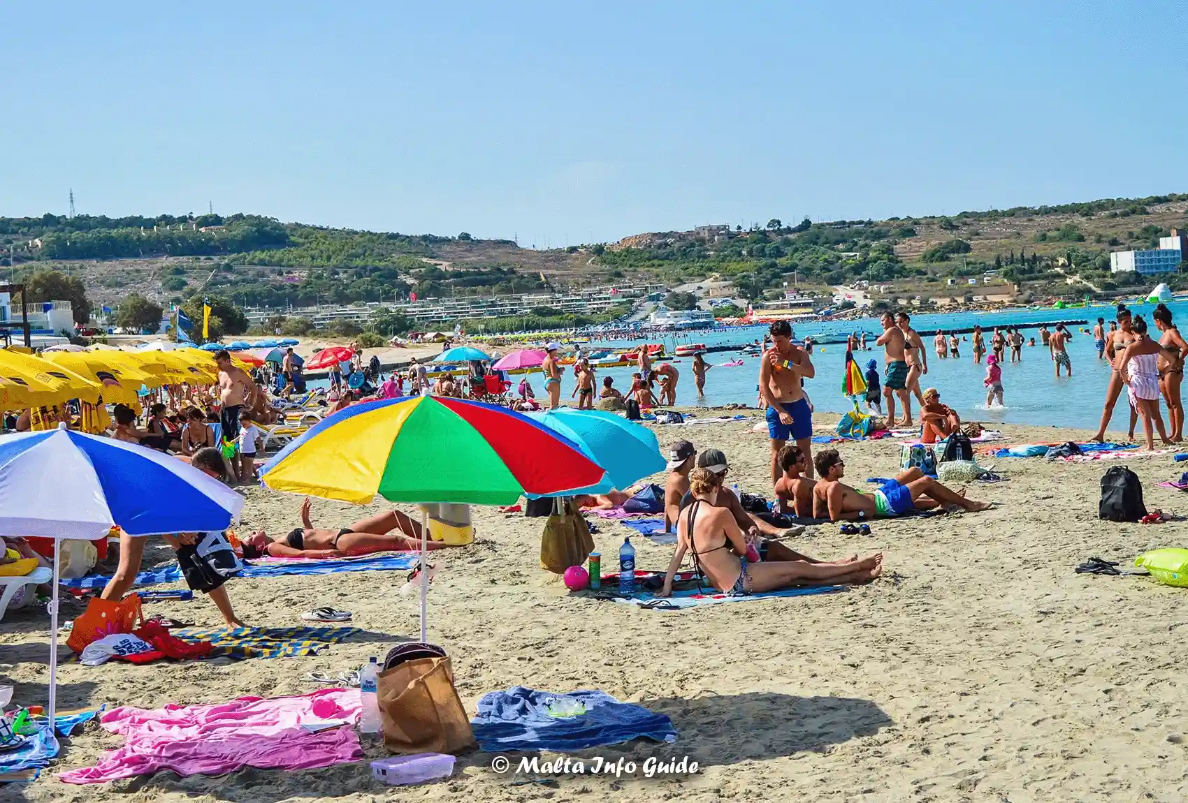 Mellieħa Bay beach, with families, swimmers, and colourful umbrellas, on a busy summer day at Għadira Bay.
