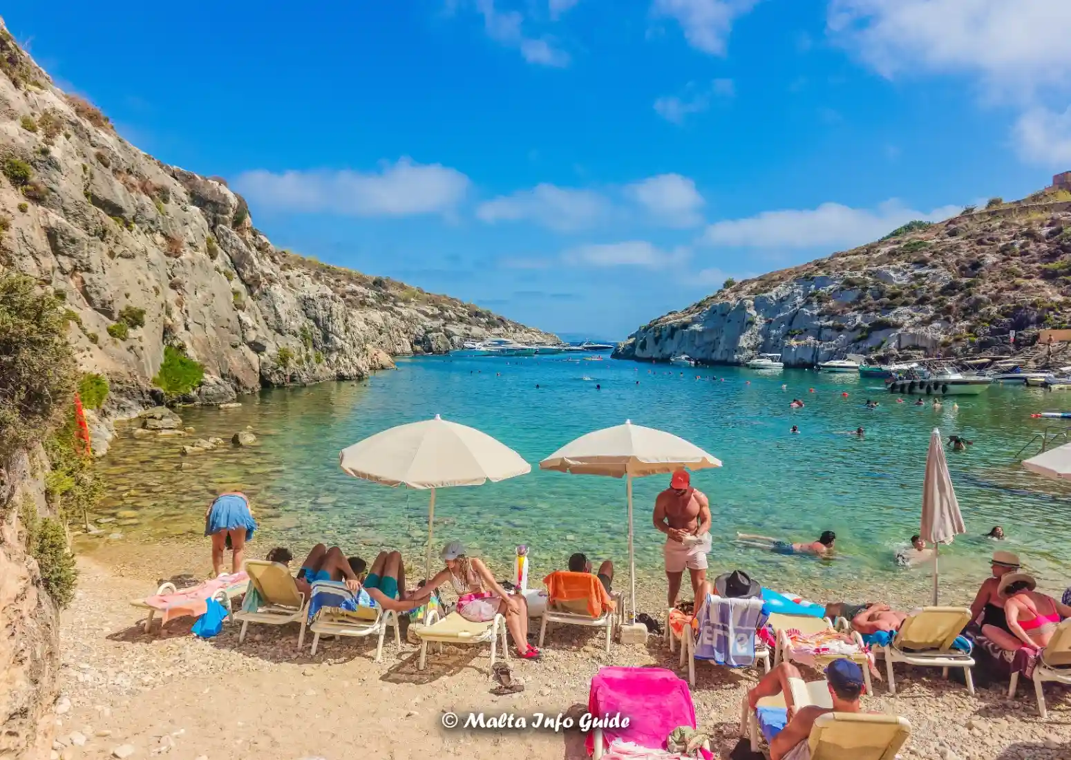 Swimmers and sunbeds line clear Mġarr ix-Xini waters.