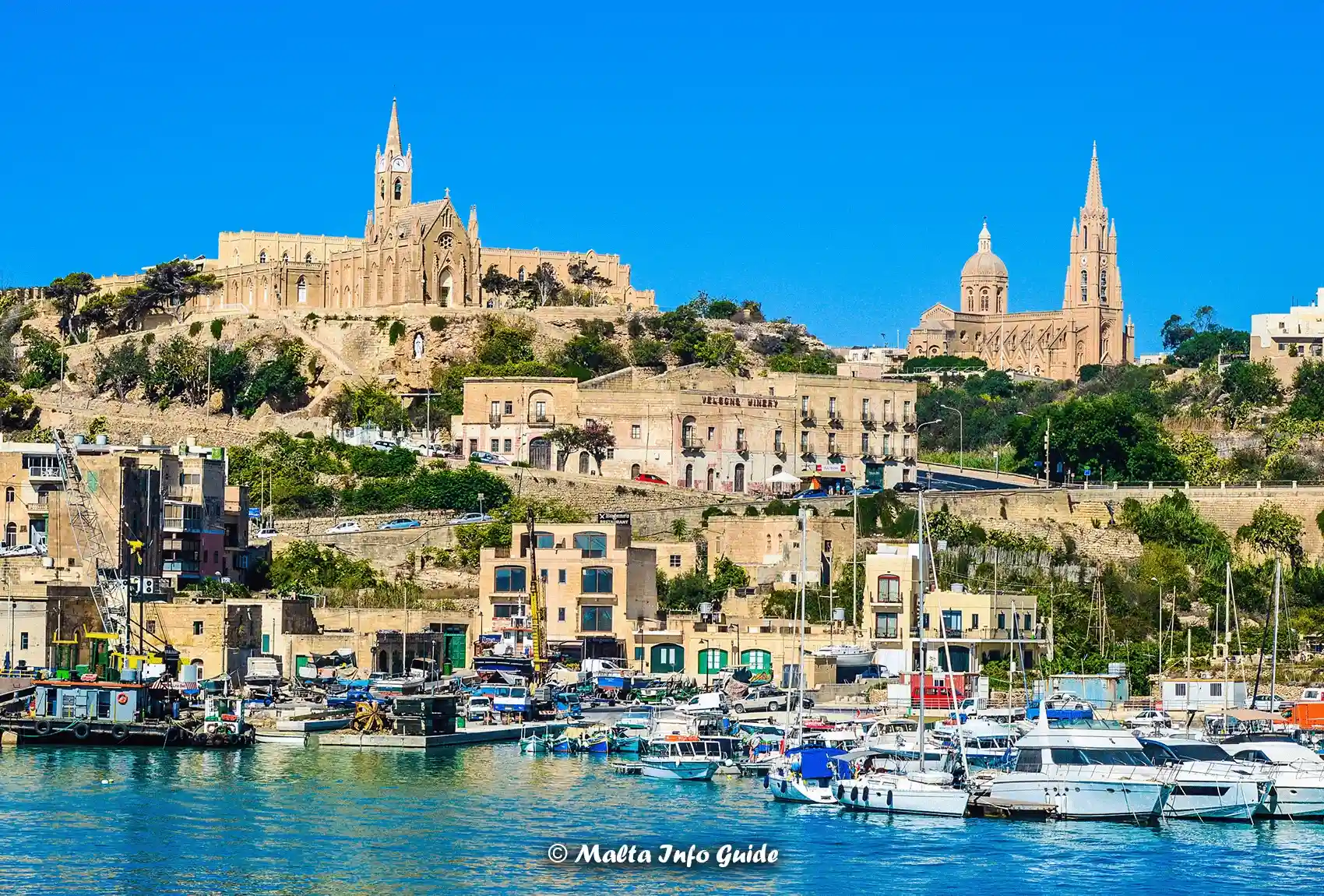 In Gozo, the picturesque Mgarr Harbour with its boats, waterfront buildings, and hilltop churches