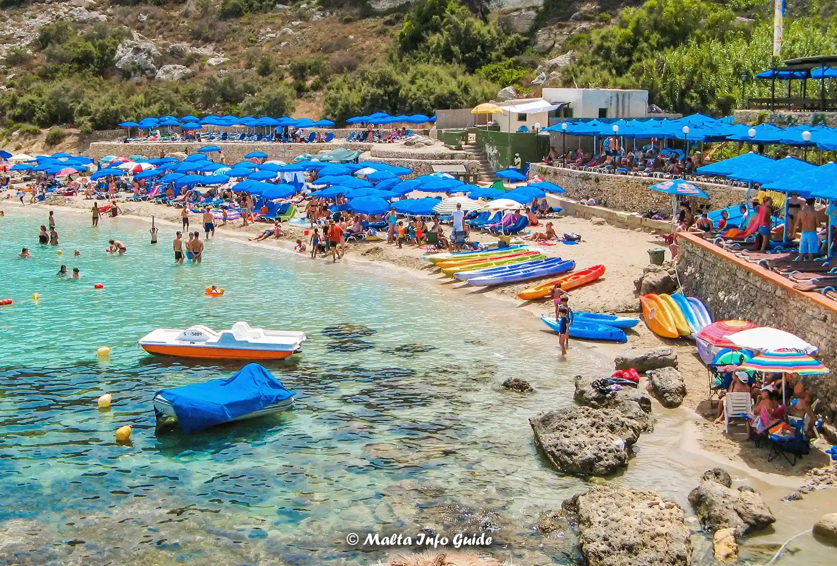 Kayaks, sunbeds and swimmers line Paradise Bay's sandy shore.