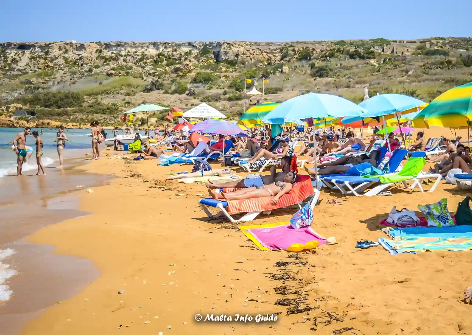 Busy Ramla Bay beach with sunbeds and umbrellas in Gozo, Malta.