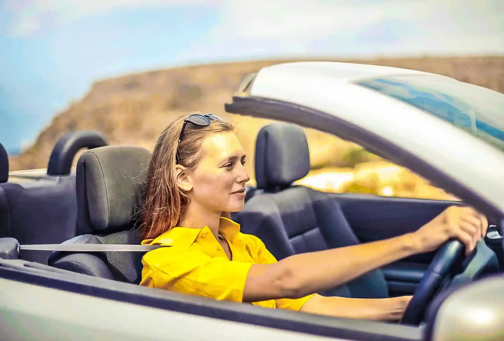 Woman driving a convertible car on sunny road.