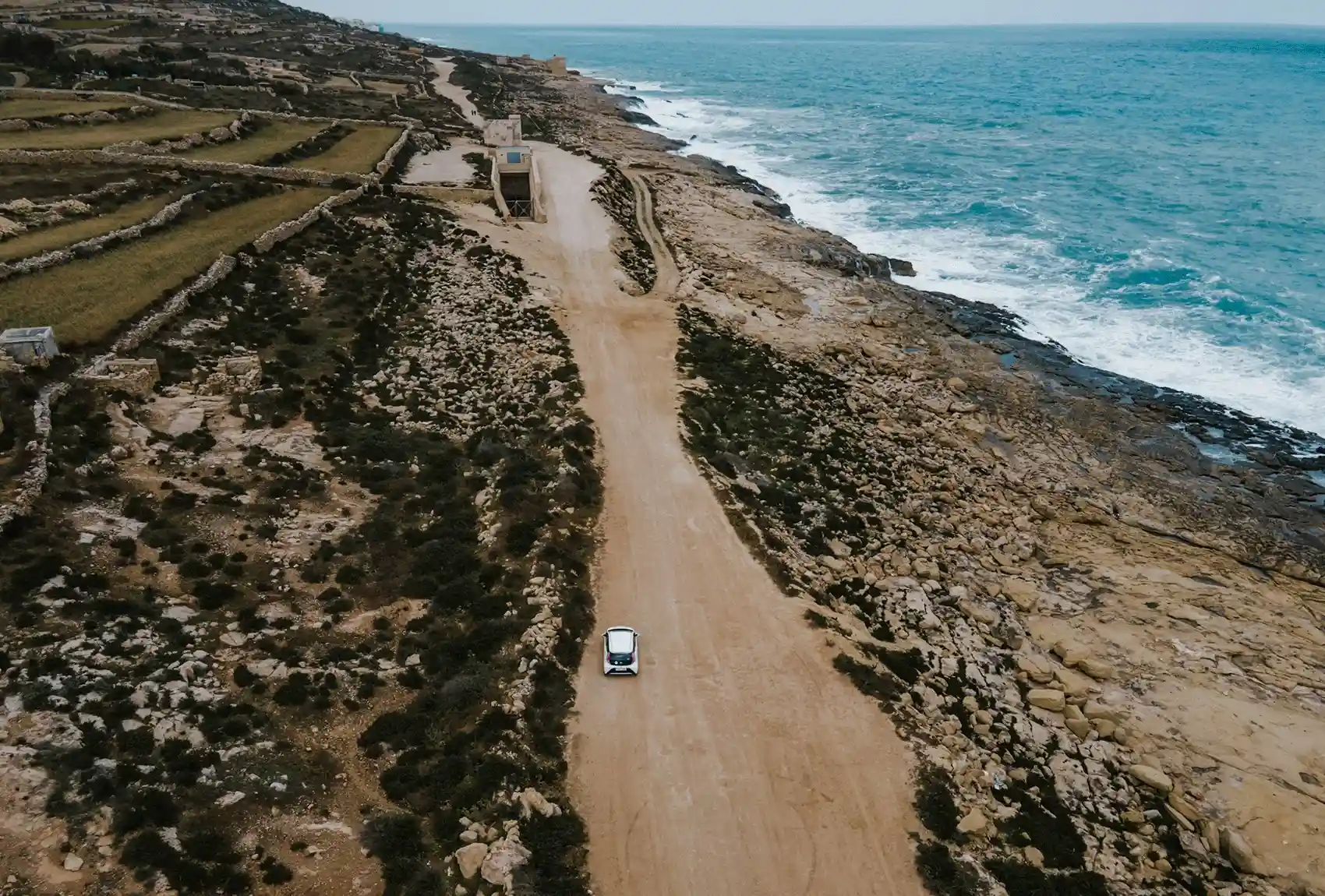 White car driving along a rocky Malta coastline.