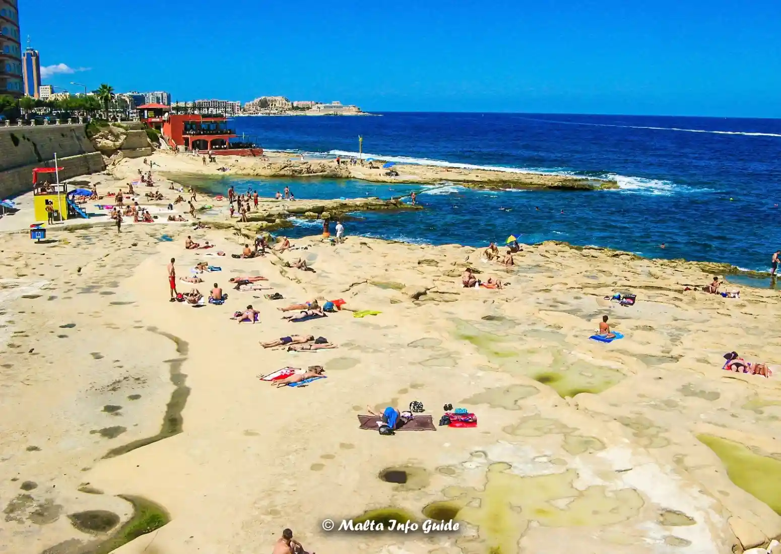 Sunbathers relax on Sliema’s broad rocky swimming coast.
