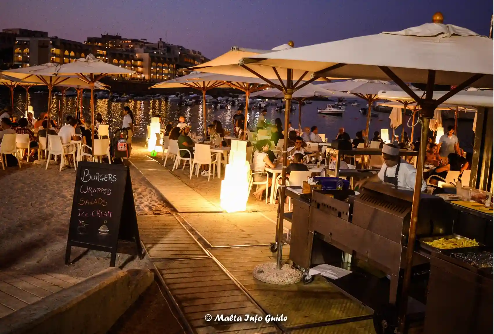 Diners seated under umbrellas beside St George's Bay.