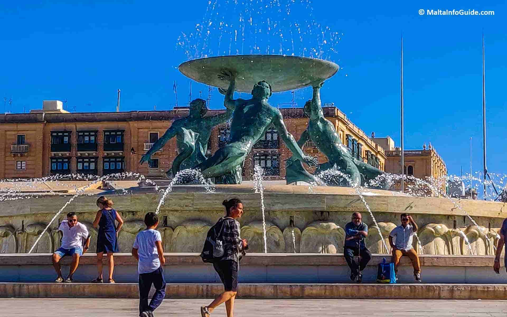 People walking past the Triton fountain just before entering the city of Valletta.