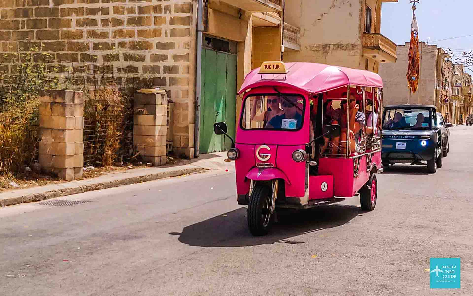 A pink Tuk Tuk with tourists driving through Xewkija Gozo streets.