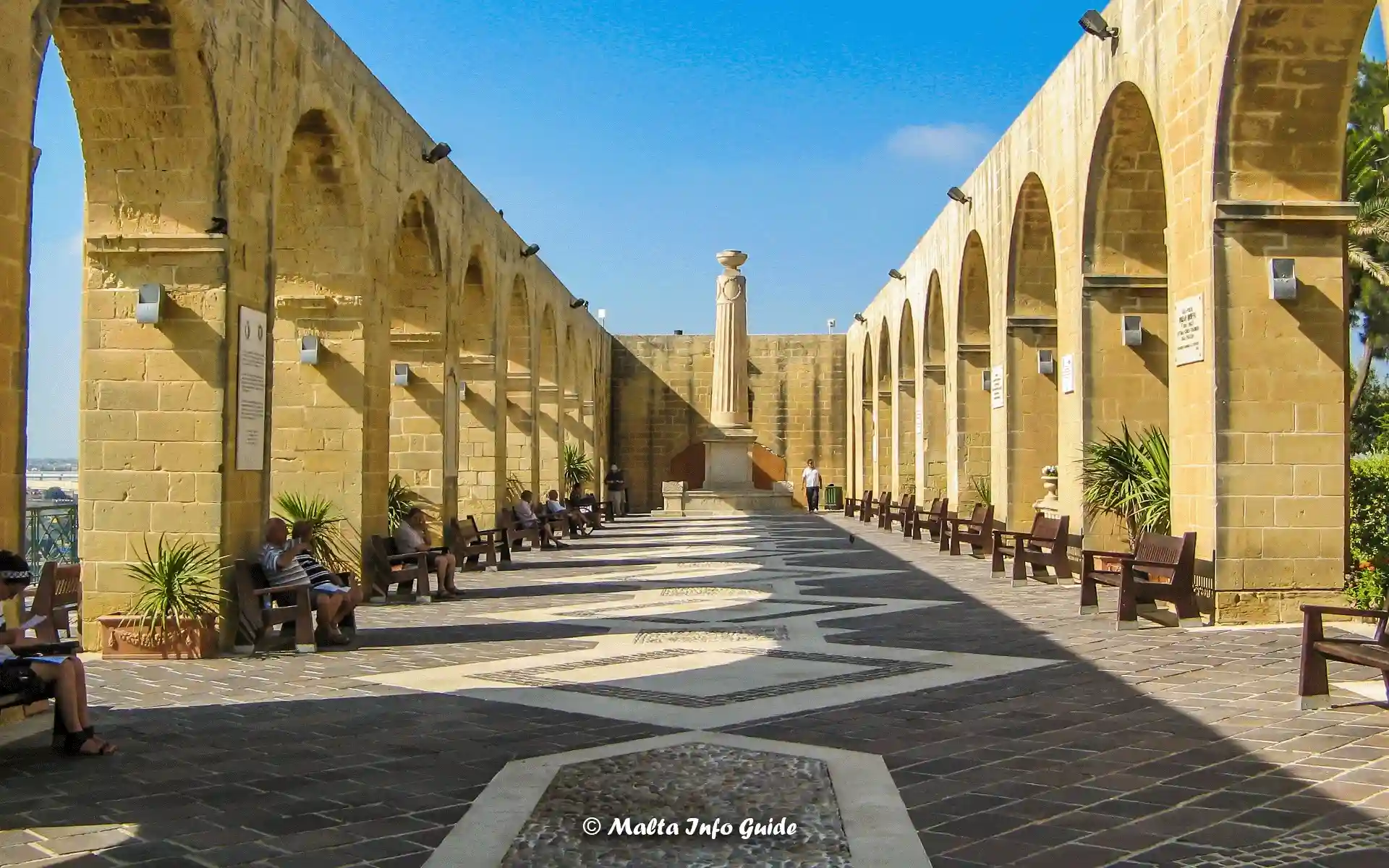 The rays of light at sunrise shining at Upper Barrakka Gardens Valletta. People sitting on benches at Upper Barrakka Gardens in Valletta.