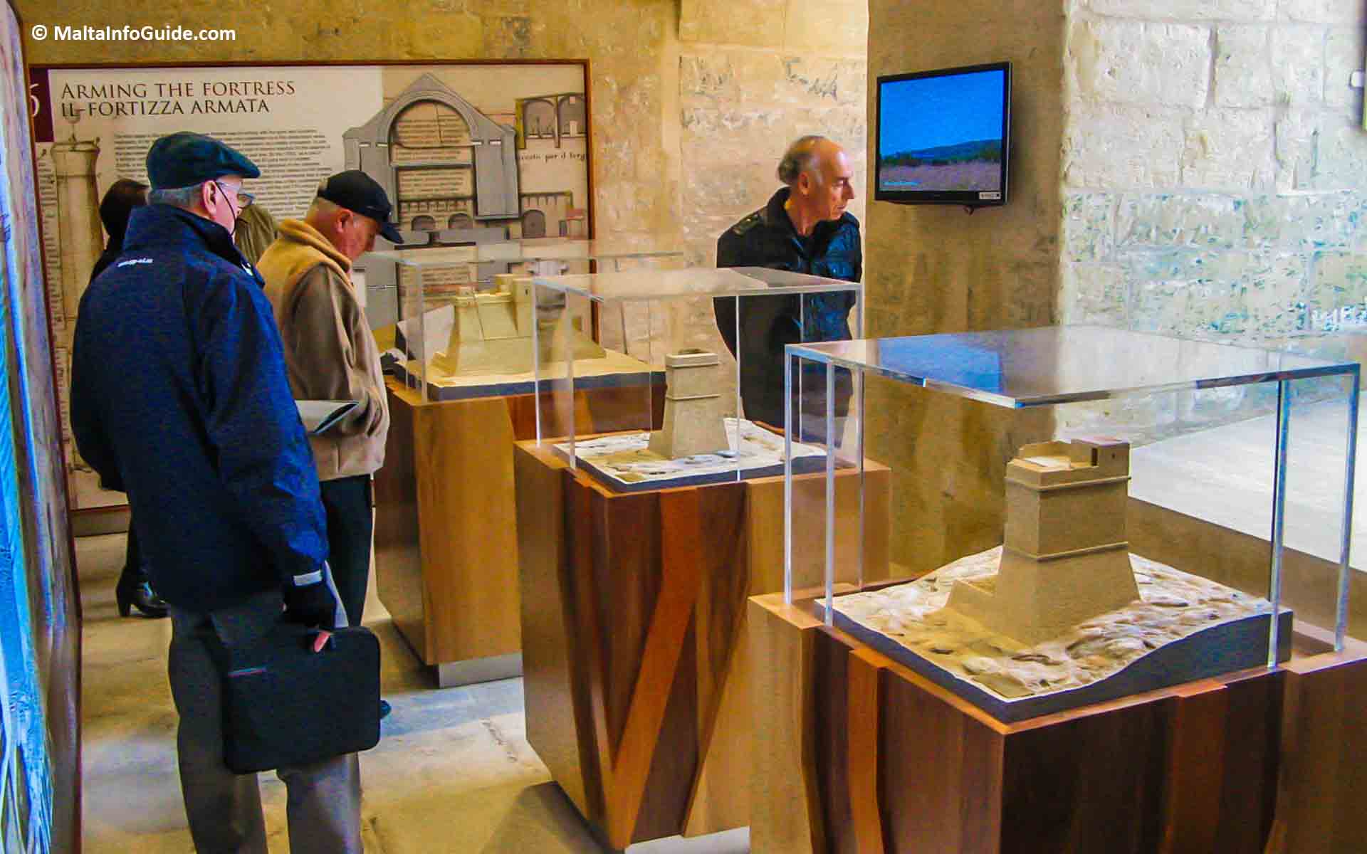 Three men walking around a room having a look at the models.