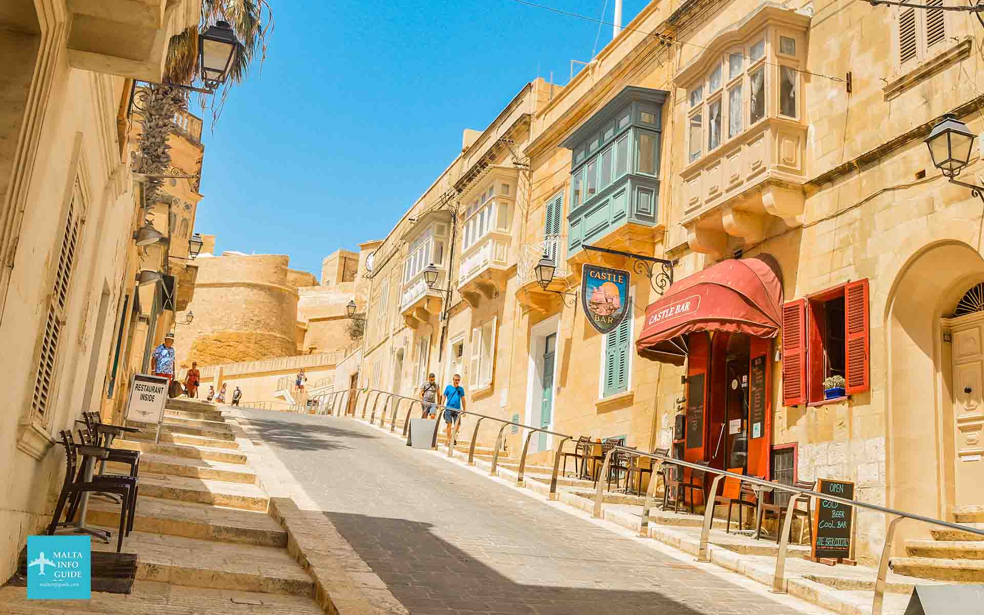 Una pittoresca strada di Victoria, Gozo, con i tradizionali balconi Maltesi e la storica Cittadella sullo sfondo.