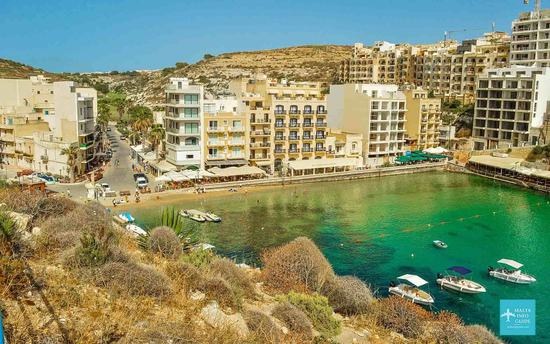 Aerial view of Xlendi Bay with boats, buildings, and clear blue water.