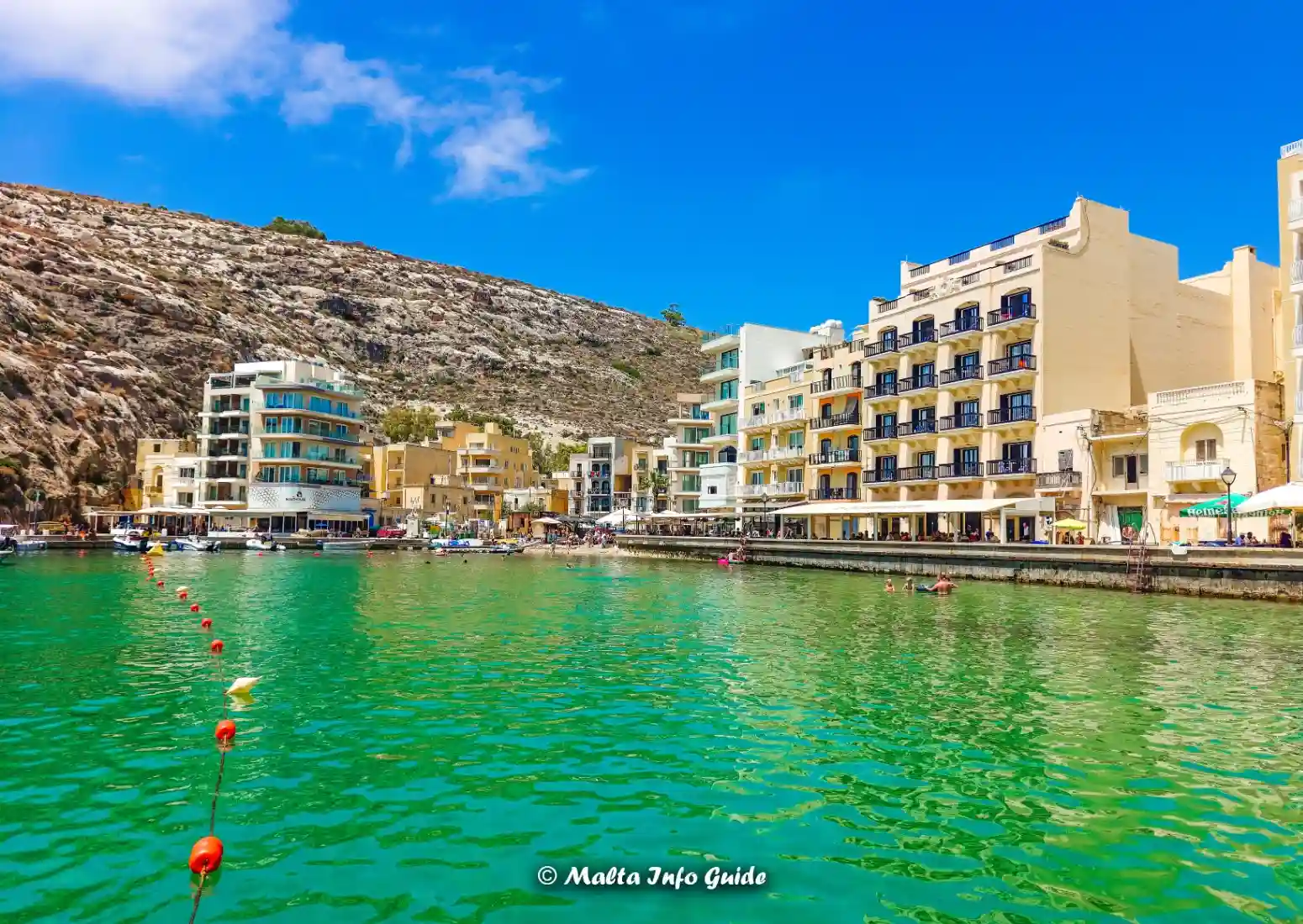 Xlendi Bay in Gozo with waterfront buildings and swimmers.